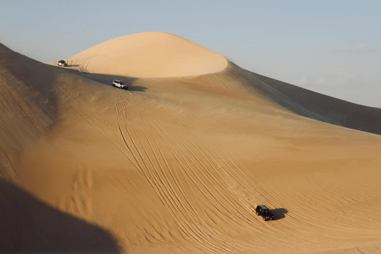 three cars in the sand with one jeep driving uphill