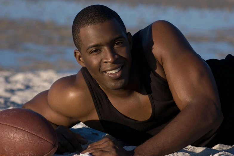 a man in black shirt laying on beach next to ball
