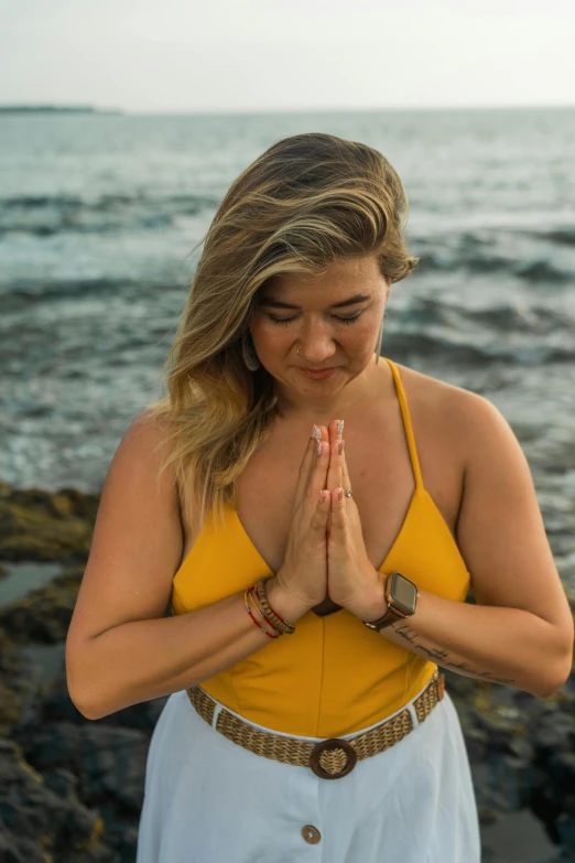 a woman sitting in front of the ocean praying