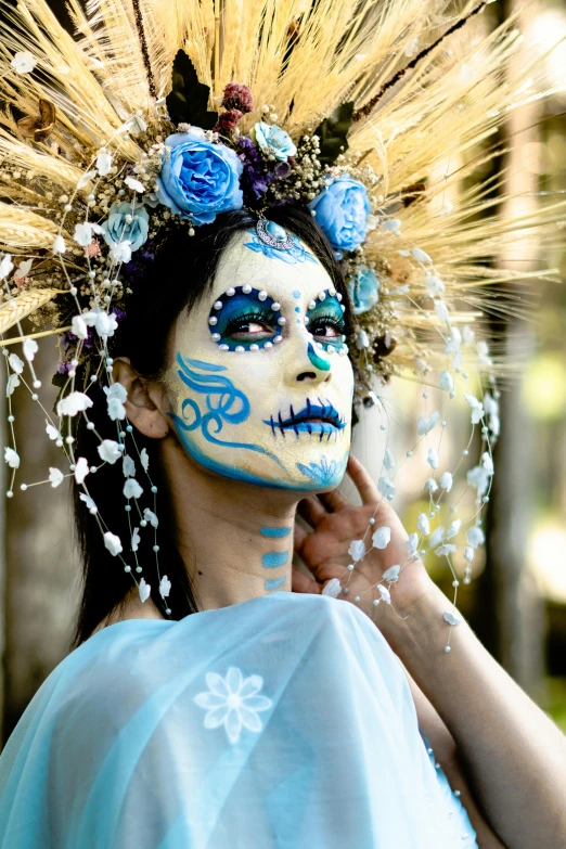a woman with a blue face painted as a flower and holding some white feathers