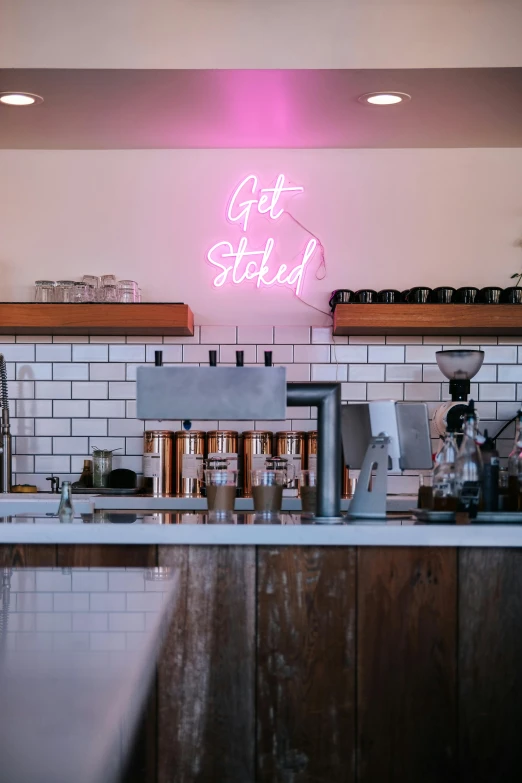 a pink neon sign behind a counter next to a coffee maker