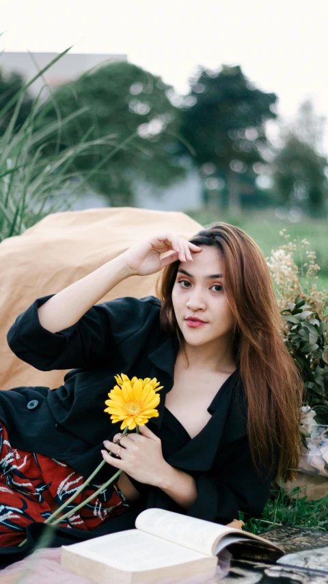 the woman in a black top sits by herself near a yellow flower