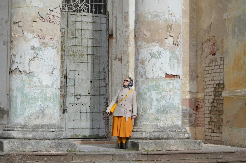 a woman in a beige top is standing by an old building