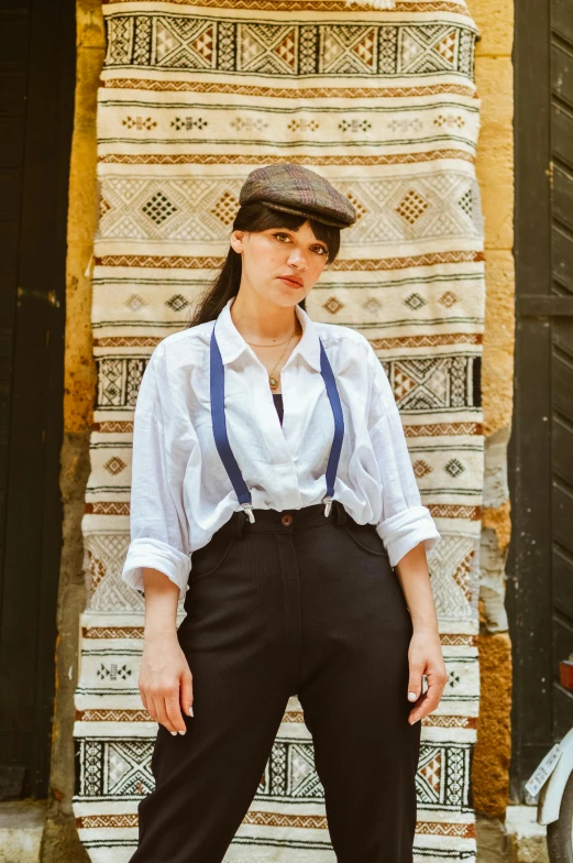 a woman in a tie and hat stands in front of a wall