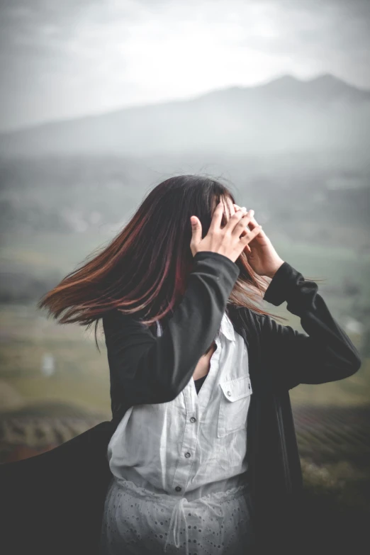 a person with long hair wearing a black jacket standing on a hill