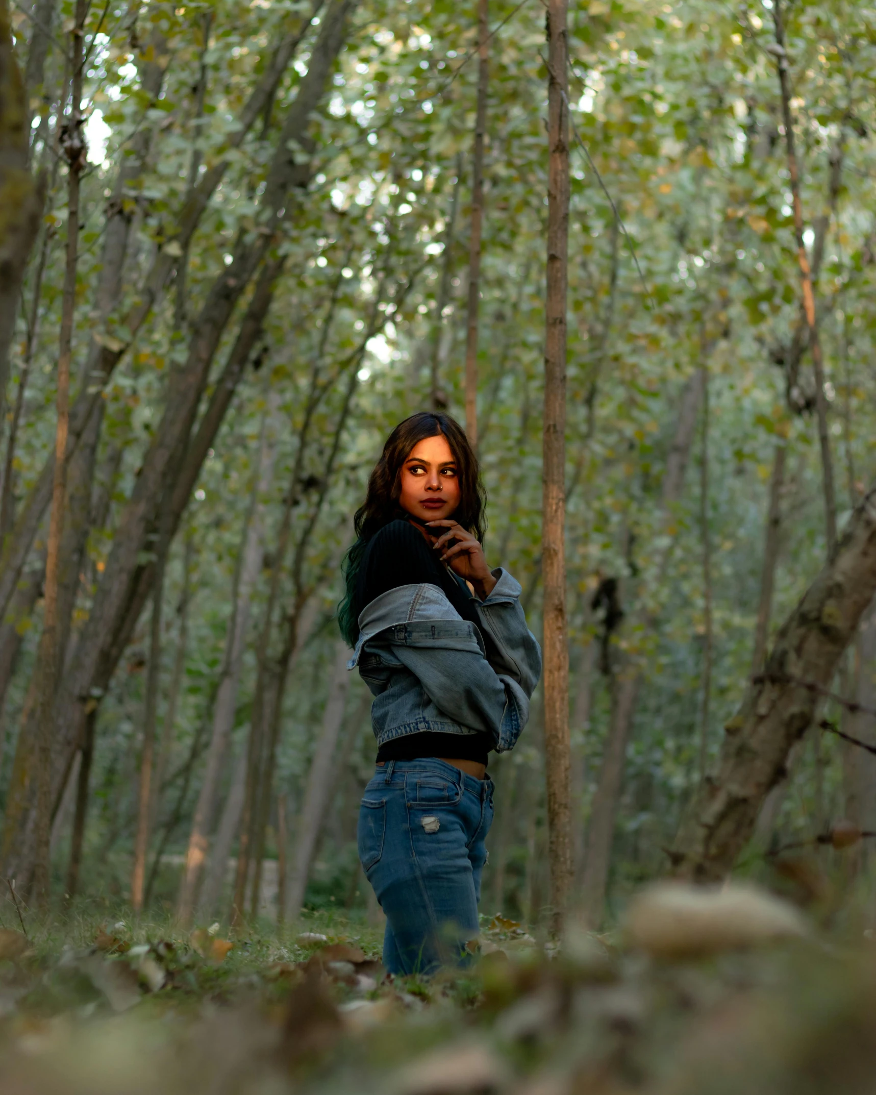 the woman is standing in a forest looking at the camera