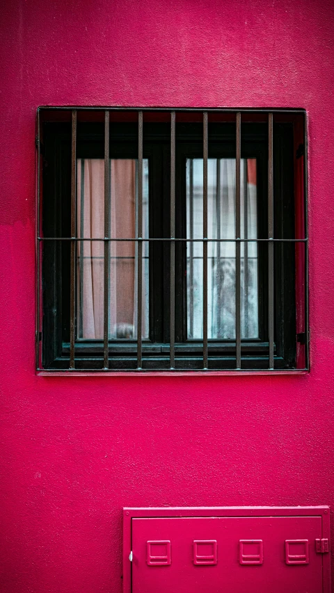 a pink wall with bars and windows reflecting the sky