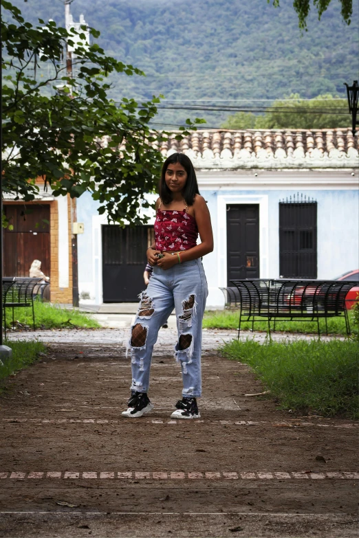 a woman in a floral shirt, ripped jeans and sneakers is standing with a baseball bat