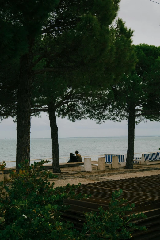 two people sit on some benches near the ocean