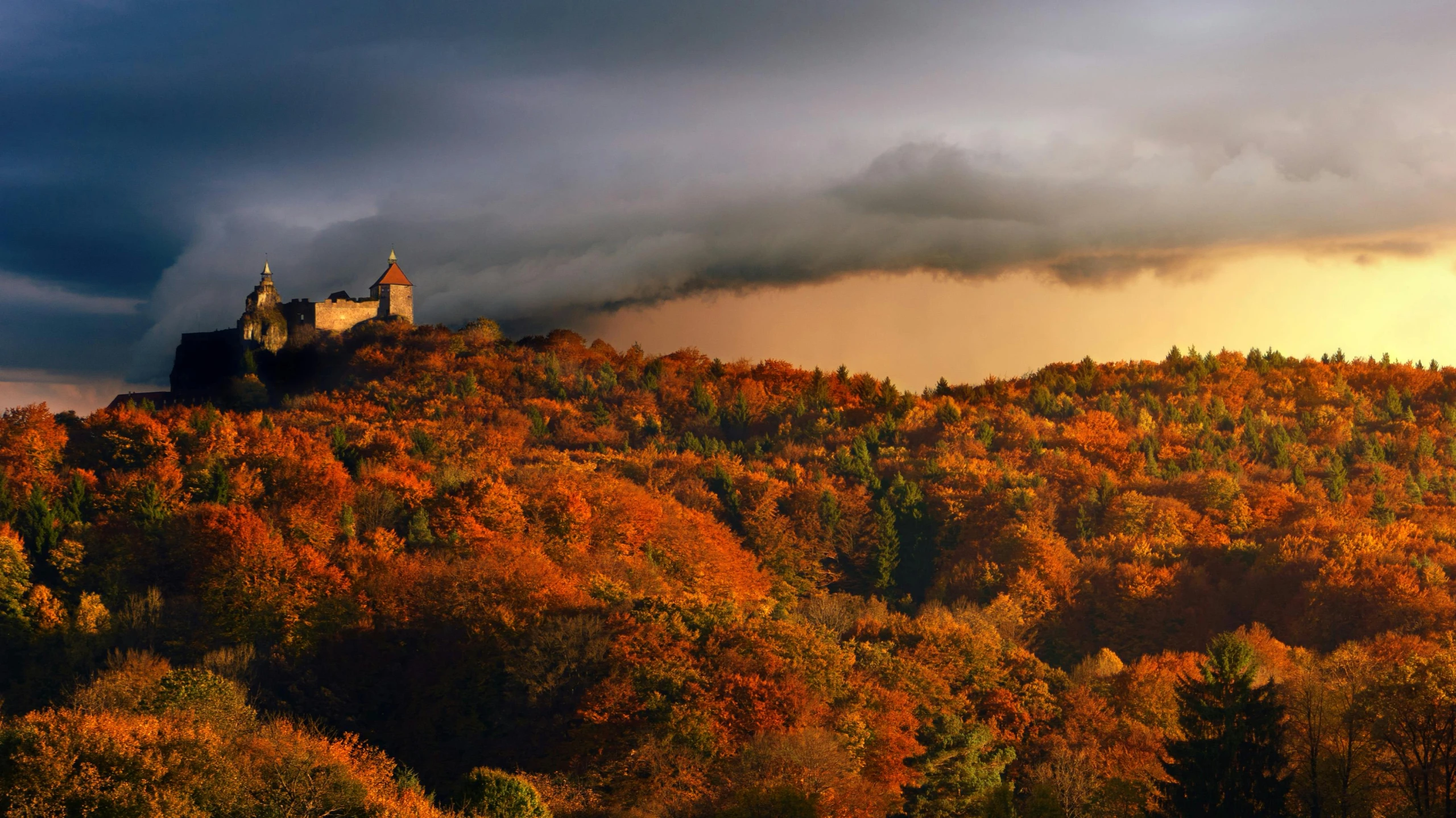 the castle has a tower on top of it near trees with oranges and browns