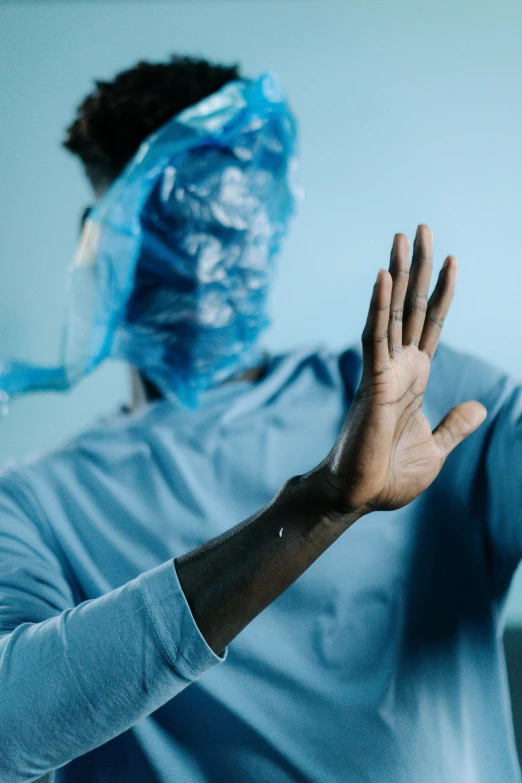 a man in a blue shirt holds his hand up while wearing a face mask