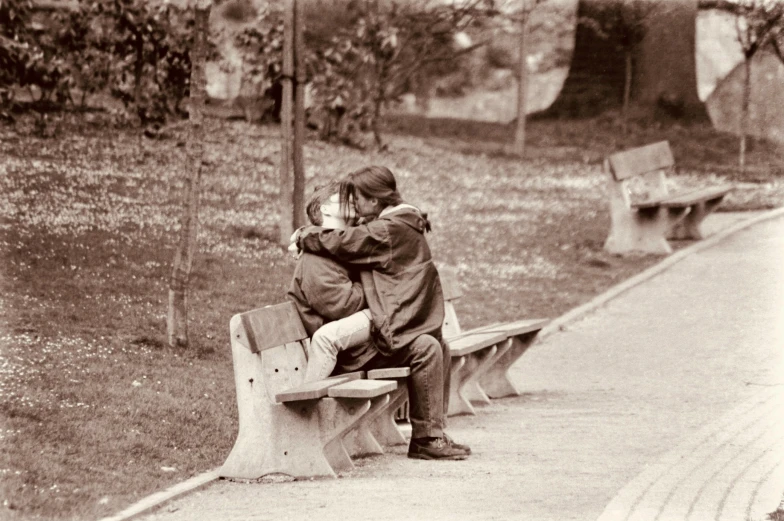 two people in park one is hugging another on a bench