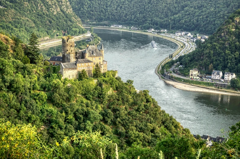 the view from the top of a mountain looking over a river with houses on the banks