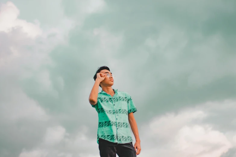 a young man in a short sleeved shirt looks up into the cloudy sky