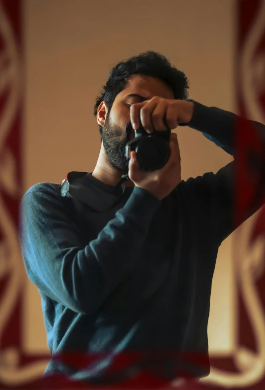 a man holds a camera with his right hand as he takes a picture of himself in the mirror