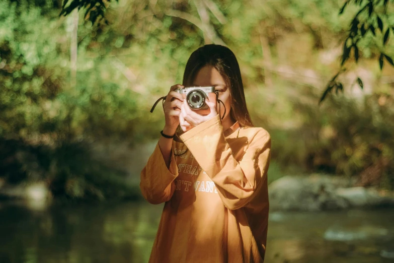 a woman is holding a camera while standing near some water