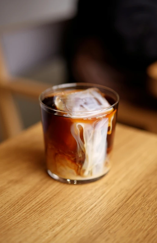 a s glass with some liquid sitting on top of a wooden table