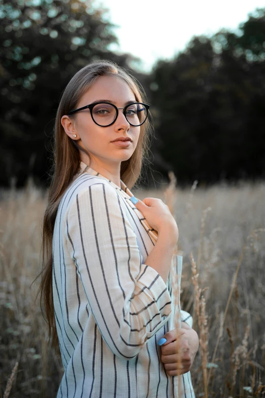 the woman stands in tall grass wearing round sunglasses