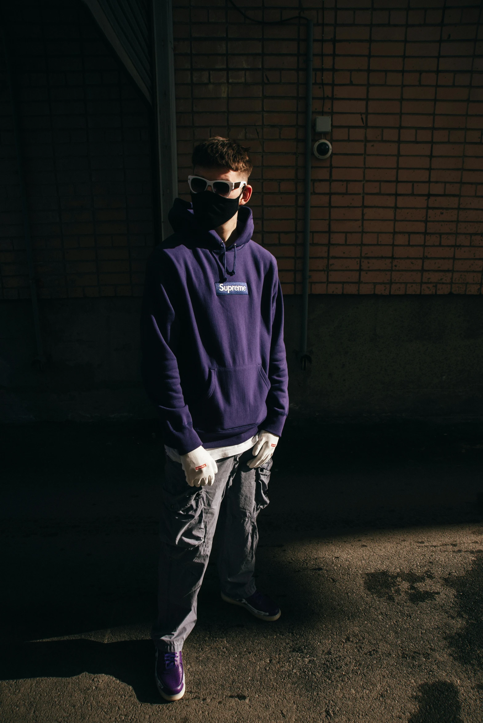 a young man wearing a mask and hoodie standing in a dark alley