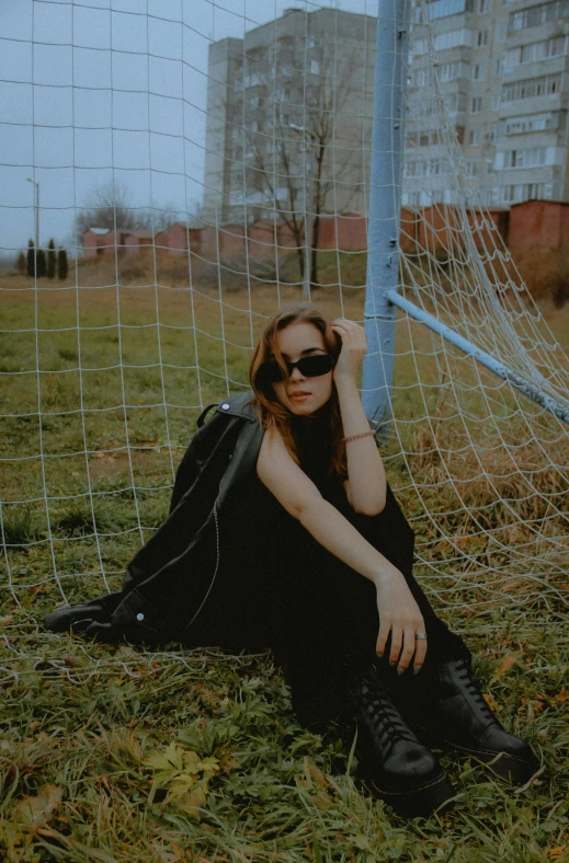 woman with eye glasses sitting on grass with soccer goal in background