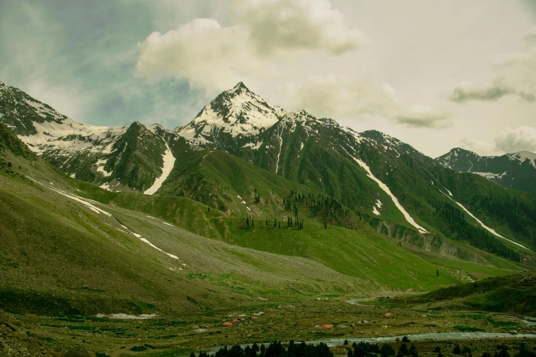 the mountains in a green valley are covered with snow