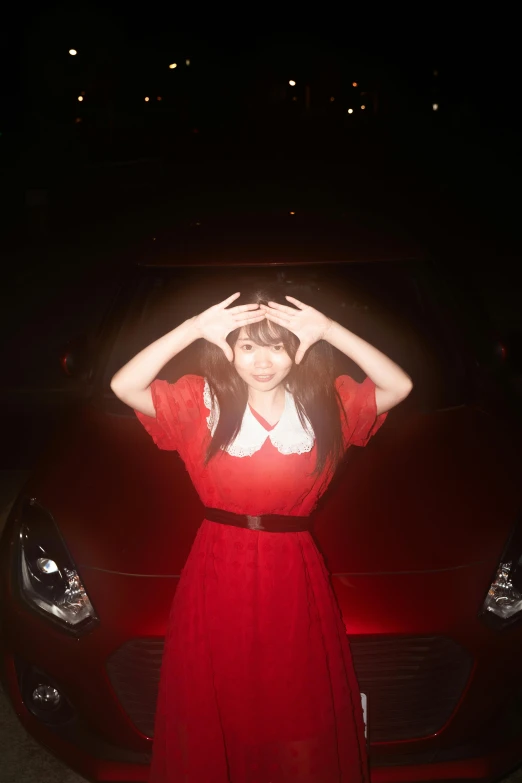 a beautiful young lady in a red dress by a dark car