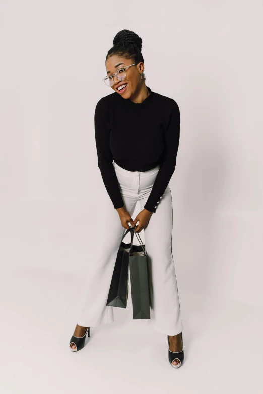 an attractive woman with glasses, black sweater, and white pants