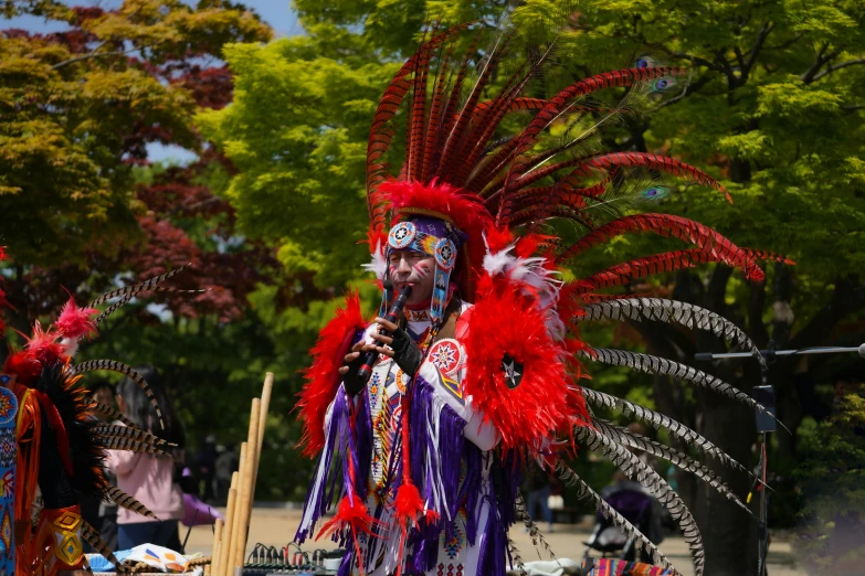 a woman with red feathers and colorful clothes holds a microphone