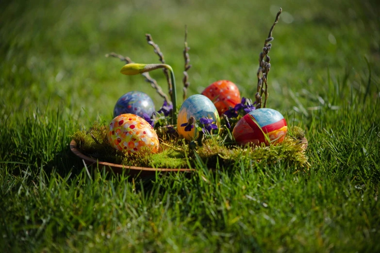 a bowl filled with painted eggs sitting in the grass