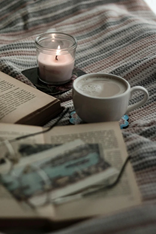 a candle sits beside an open book, cup, and a candle light