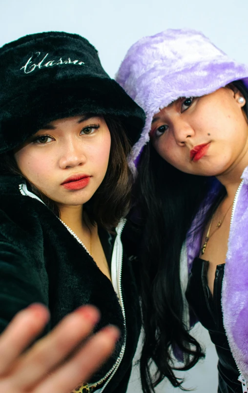 two asian women in matching hats giving a hand signal