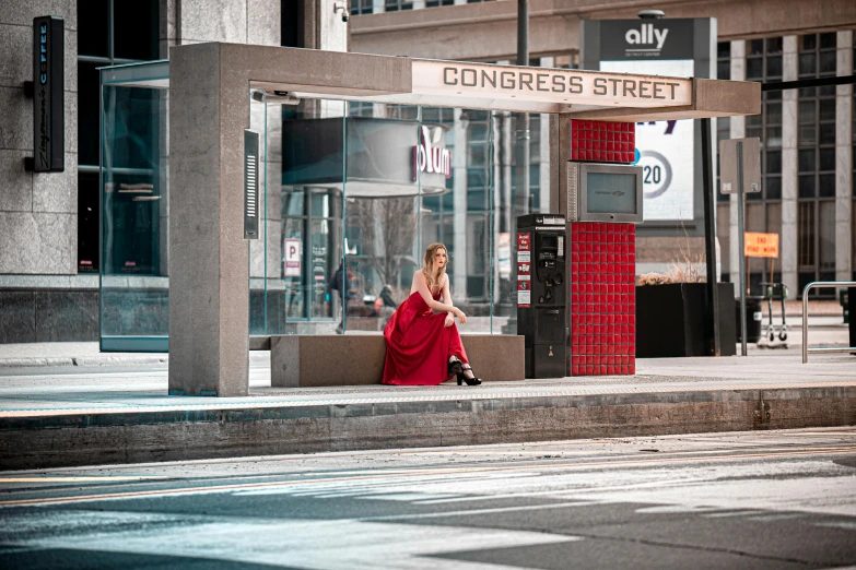 a woman in red dress sits on a city street corner