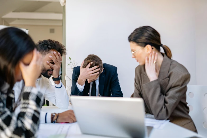 a group of people sitting around a table with their hands over their face