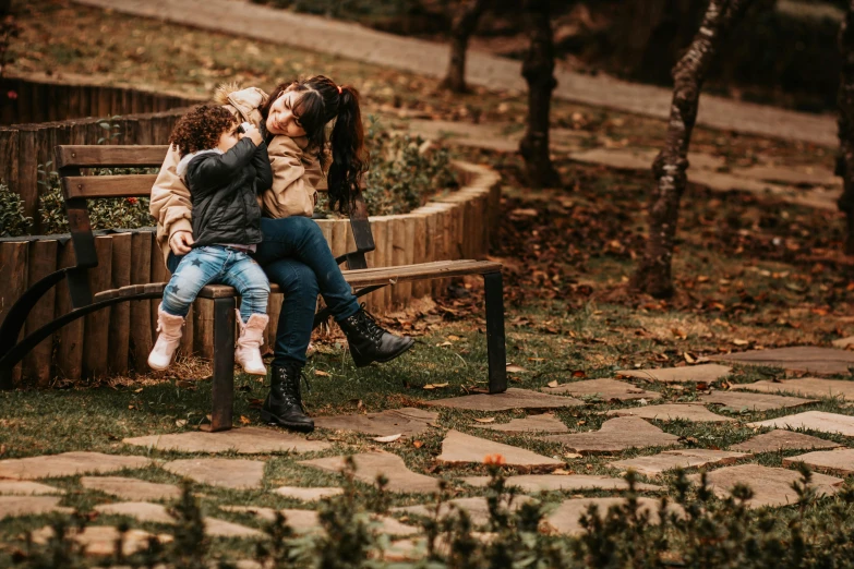 a woman sits on top of another women on a park bench