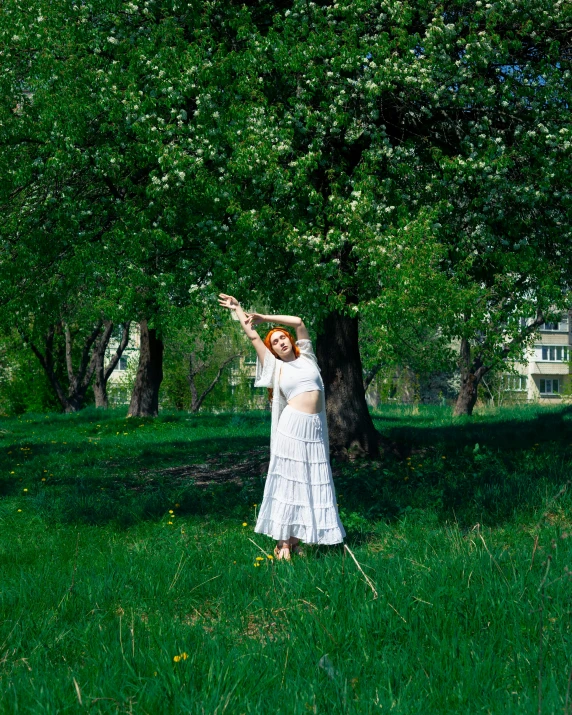 woman in white dress reaching up to a tree