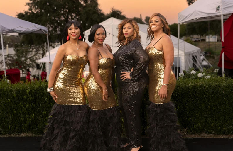 three black women in evening dresses stand next to each other