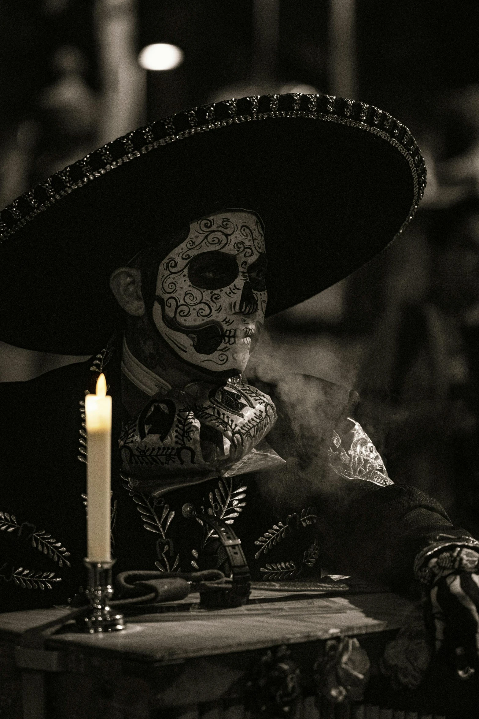 a skeleton in a sombrero smoking a cigarette while sitting next to a candle