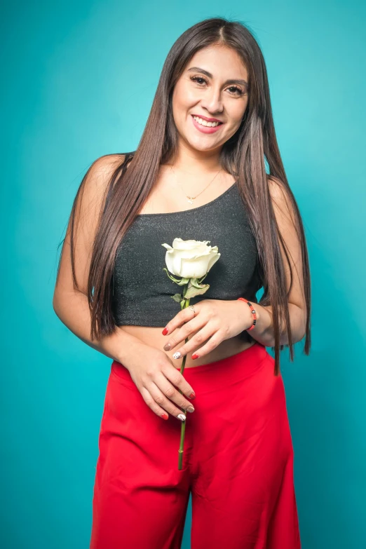 young woman wearing a black top and red pants, holding a rose
