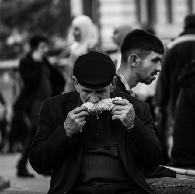 an older man is eating a sandwich with other men nearby