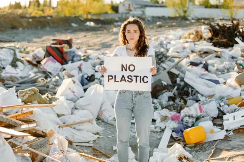 woman holding sign with no plastic sign in front of trash pile