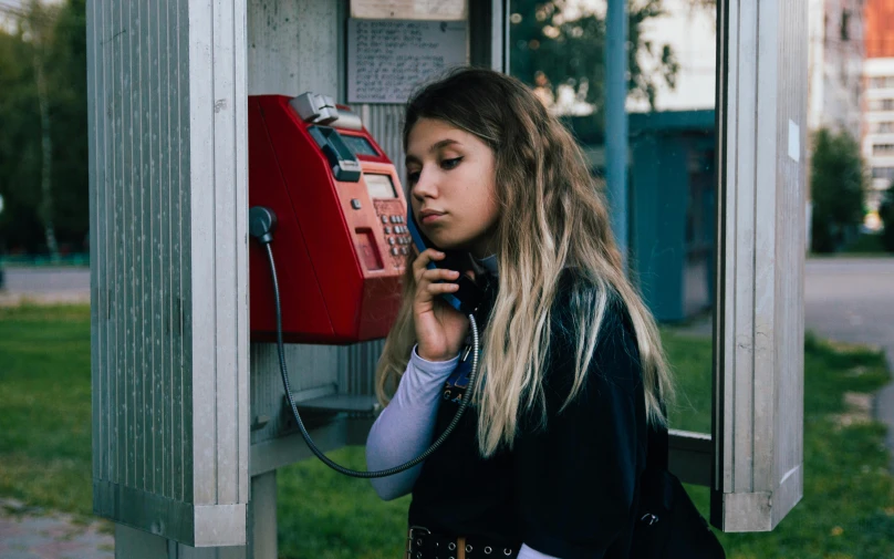 a woman in black shirt talking on phone next to telephone