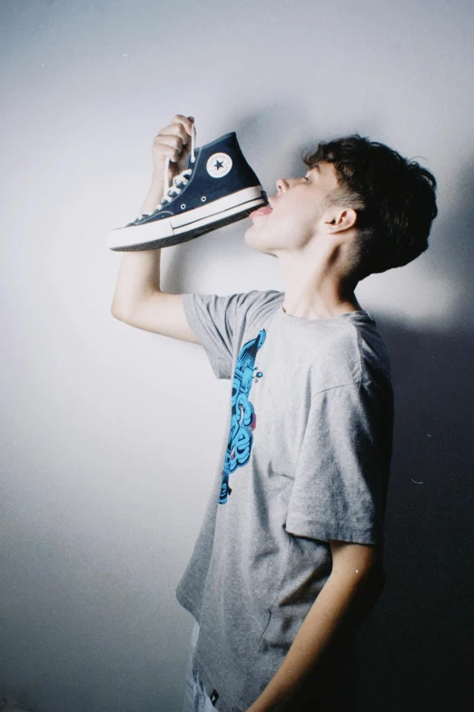 a boy drinking from a can with a sneaker on his shoe