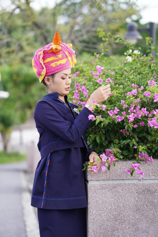 a woman wearing a purple and pink hat is standing by some flowers