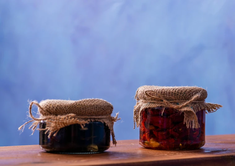 two jars of red wine sitting on top of a wooden counter