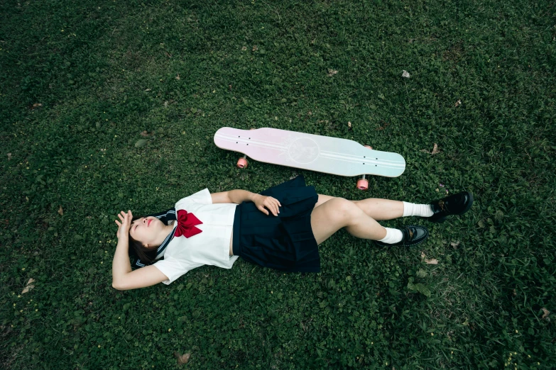 two people that are laying on the grass with a skateboard