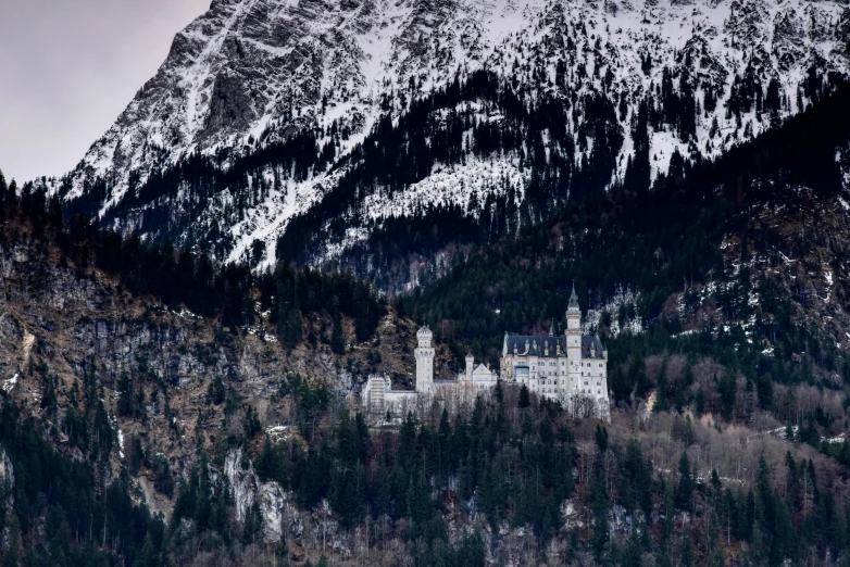 a castle stands at the base of a mountain in a forested area