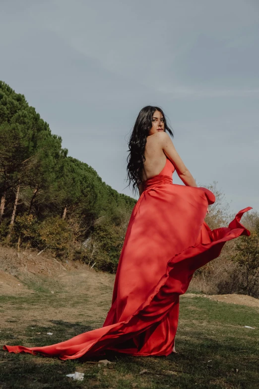 a woman in an red dress standing next to some trees