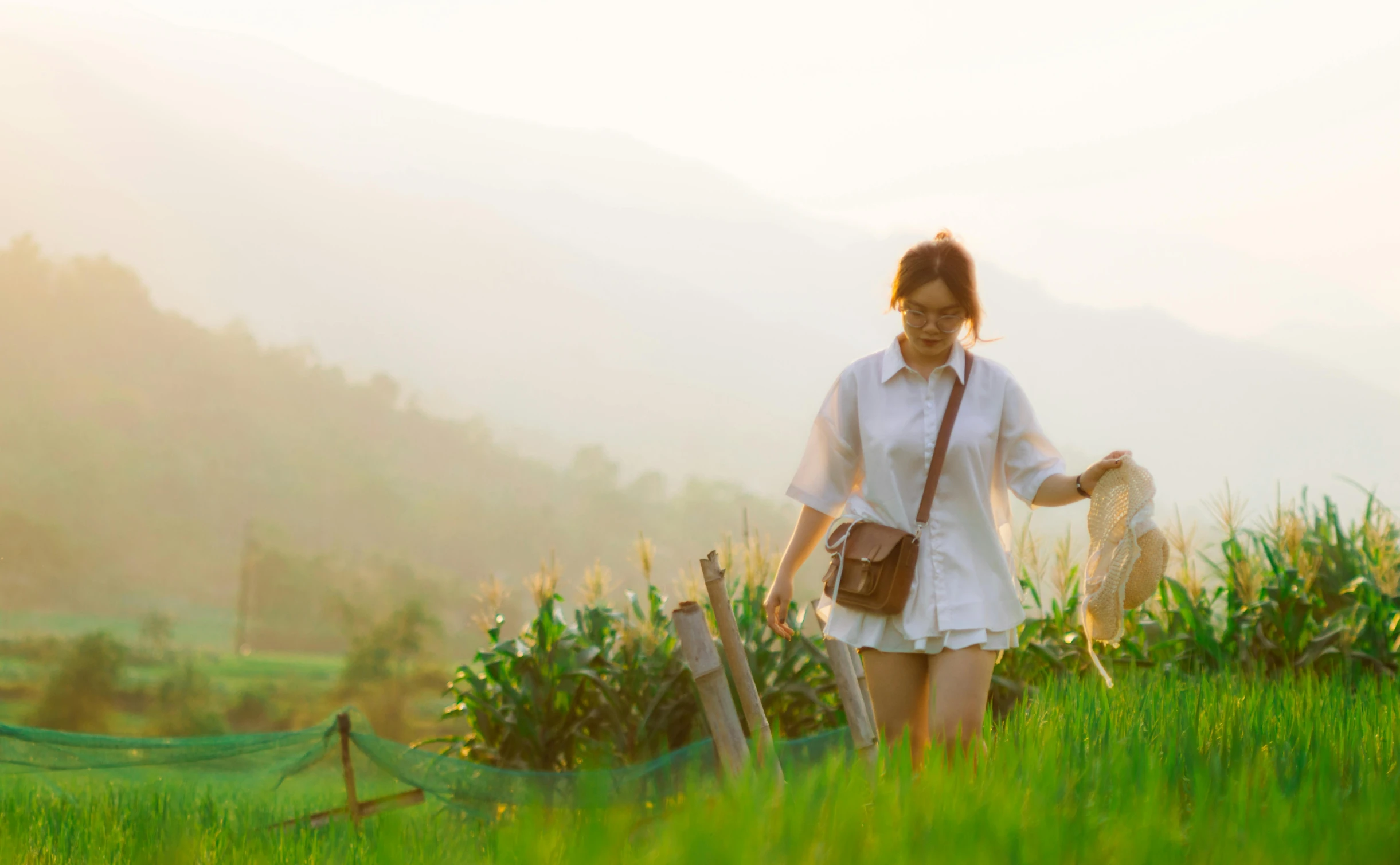 woman walking through grass while holding a bag