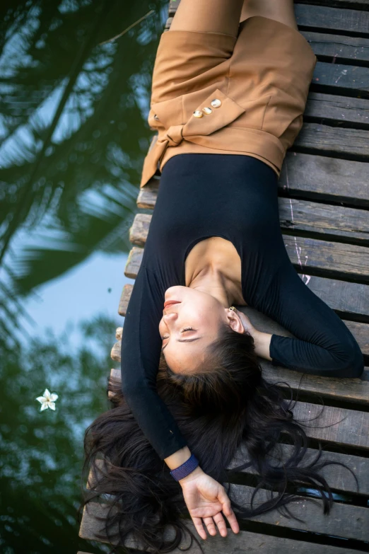 a beautiful woman laying on top of a bench next to water