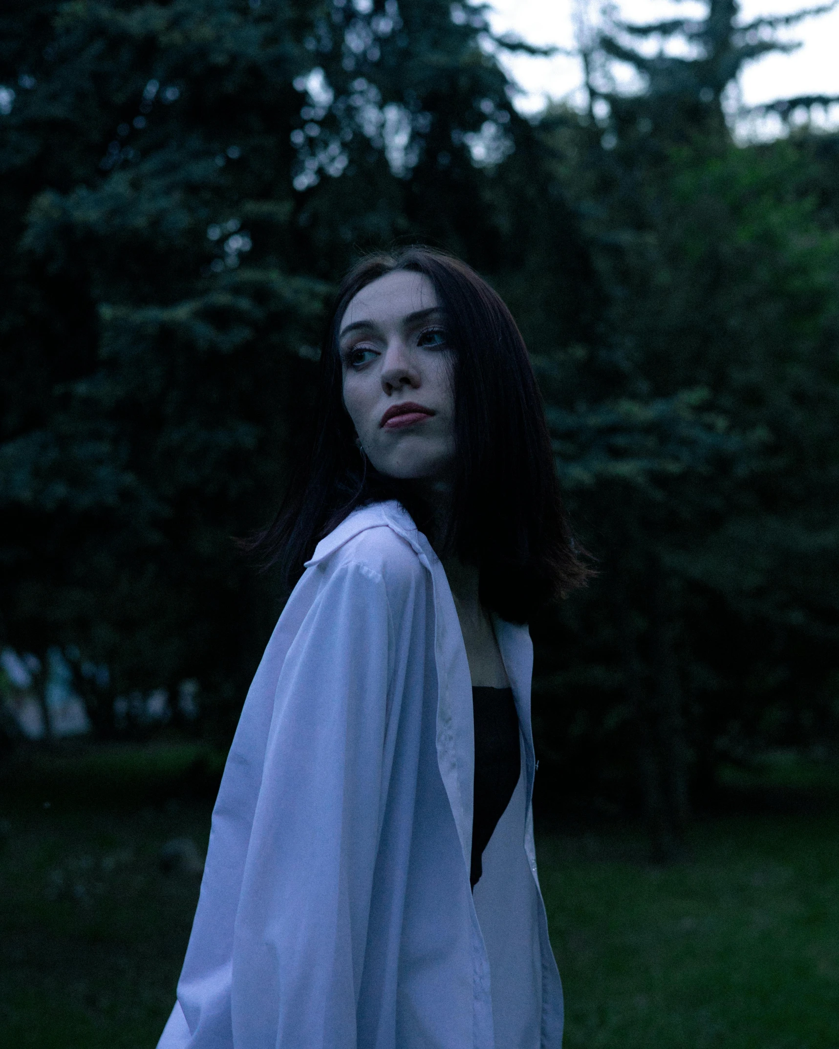 a girl with long dark hair standing in front of some trees